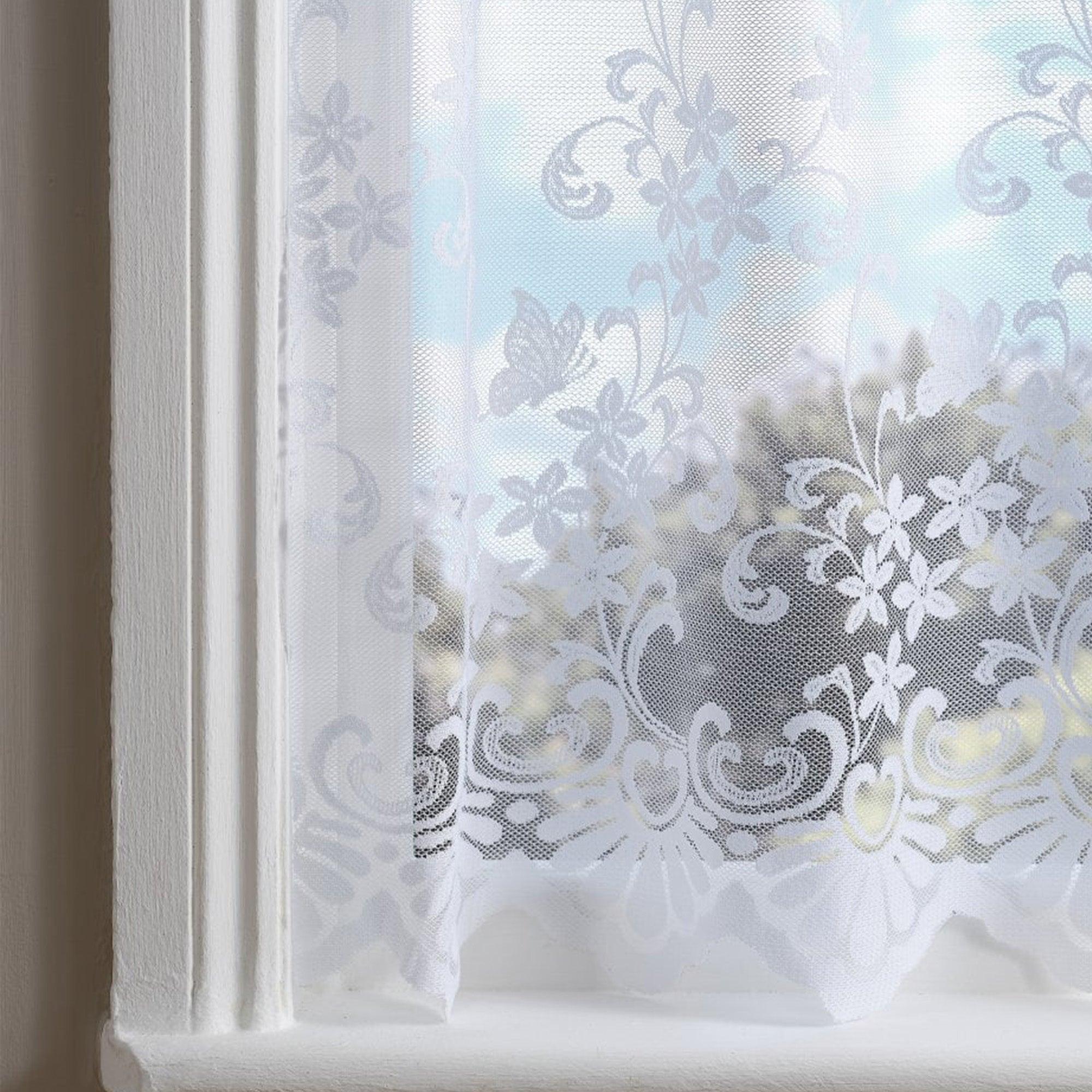 White net curtain with embroidered flowers and swirl patterns against a blurred window 