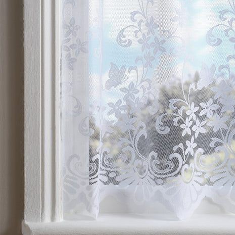 White net curtain with embroidered flowers and swirl patterns against a blurred window 