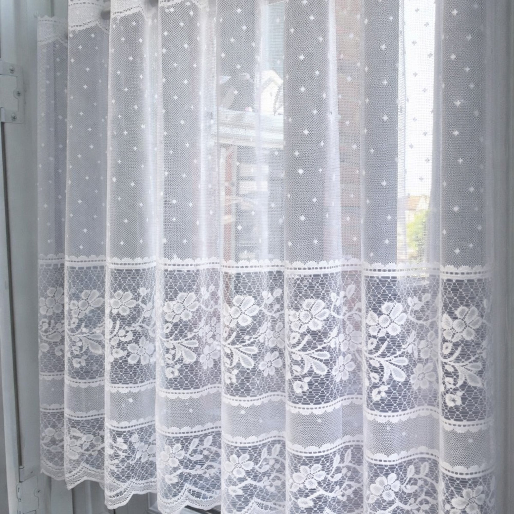 Sheer lace curtain with embroidered dots and flowers against a window 