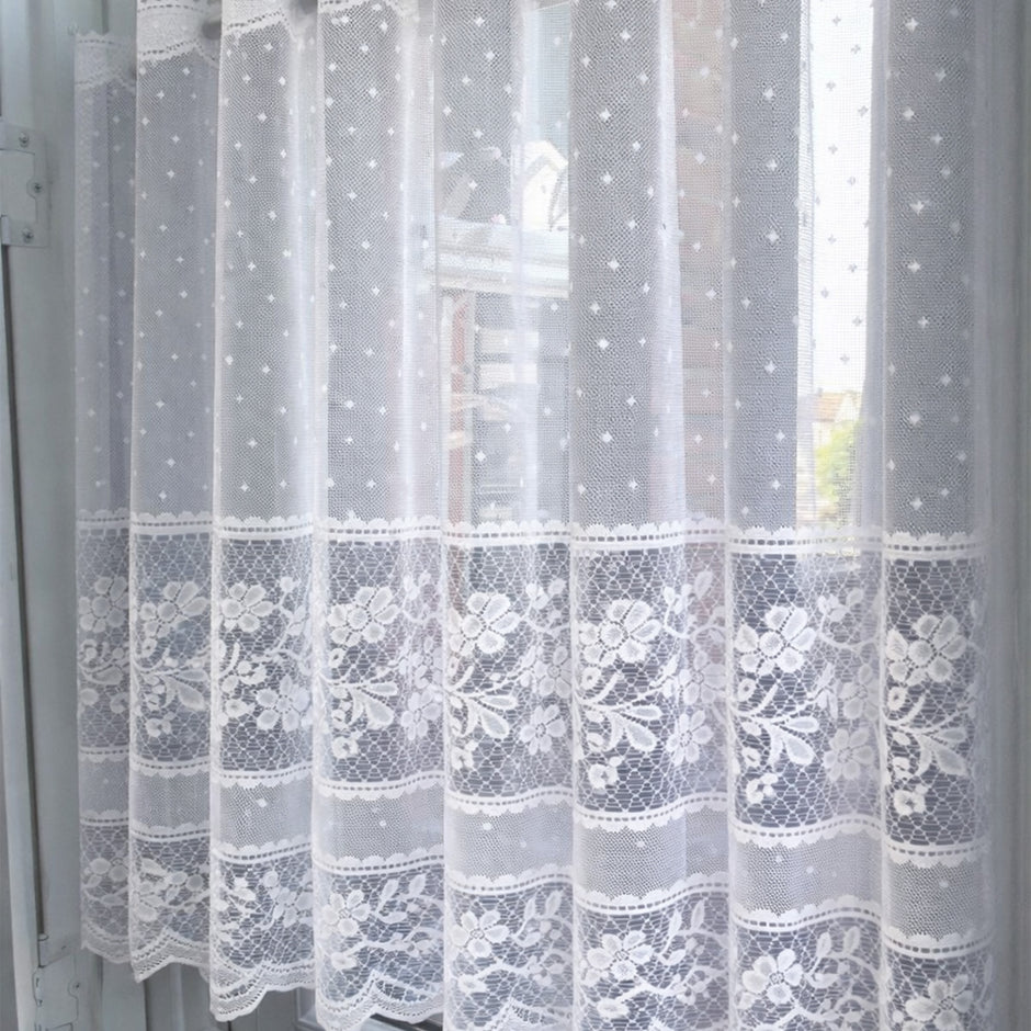 Sheer lace curtain with embroidered dots and flowers against a window 