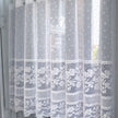 Sheer lace curtain with embroidered dots and flowers against a window 
