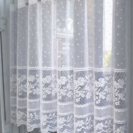 Sheer lace curtain with embroidered dots and flowers against a window 