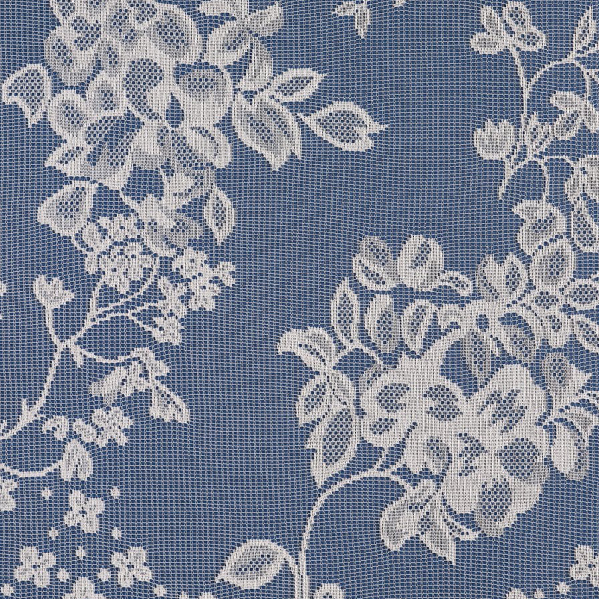 Close up of a white net curtain with embroidered flowers on a blue surface