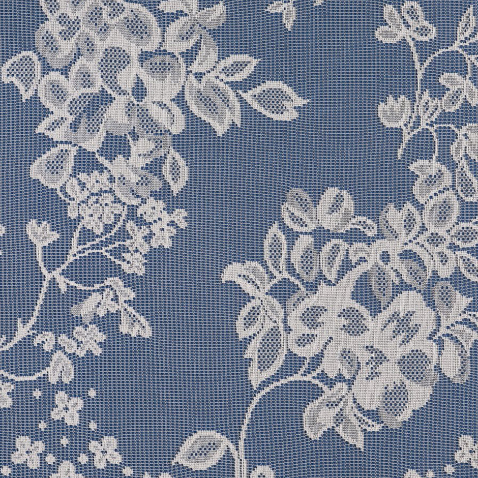 Close up of a white net curtain with embroidered flowers on a blue surface