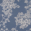 Close up of a white net curtain with embroidered flowers on a blue surface