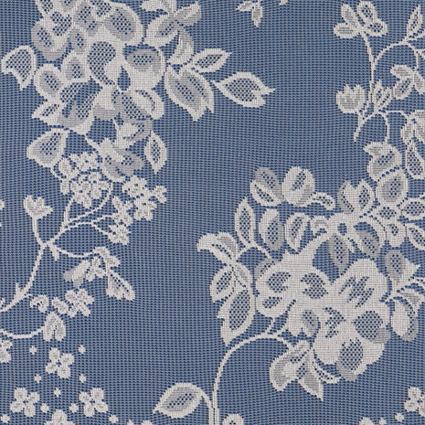 Close up of a white net curtain with embroidered flowers on a blue surface