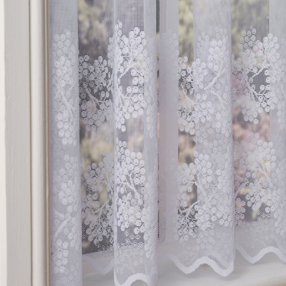 White lace curtains with floral patterns in front of a blurred outdoor background