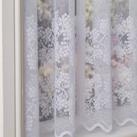 White lace curtains with floral patterns in front of a blurred outdoor background