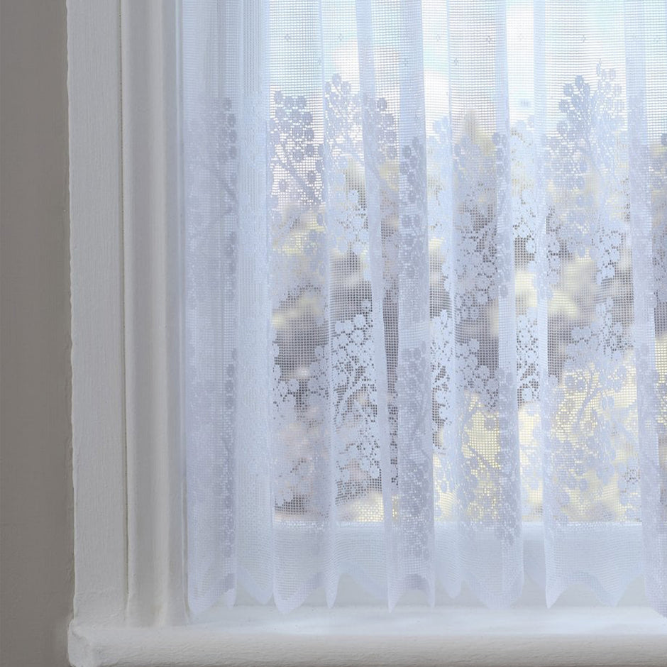 Sheer white lace curtain with floral patterns in a window setting