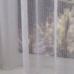 Close-up of a textured white net curtain with vertical sewn lines and dots against a blurred indoor background