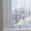 Sheer white dotty curtain in front of a window with a view of trees.