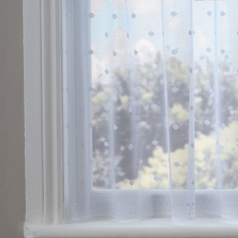 Sheer white dotty curtain in front of a window with a view of trees.