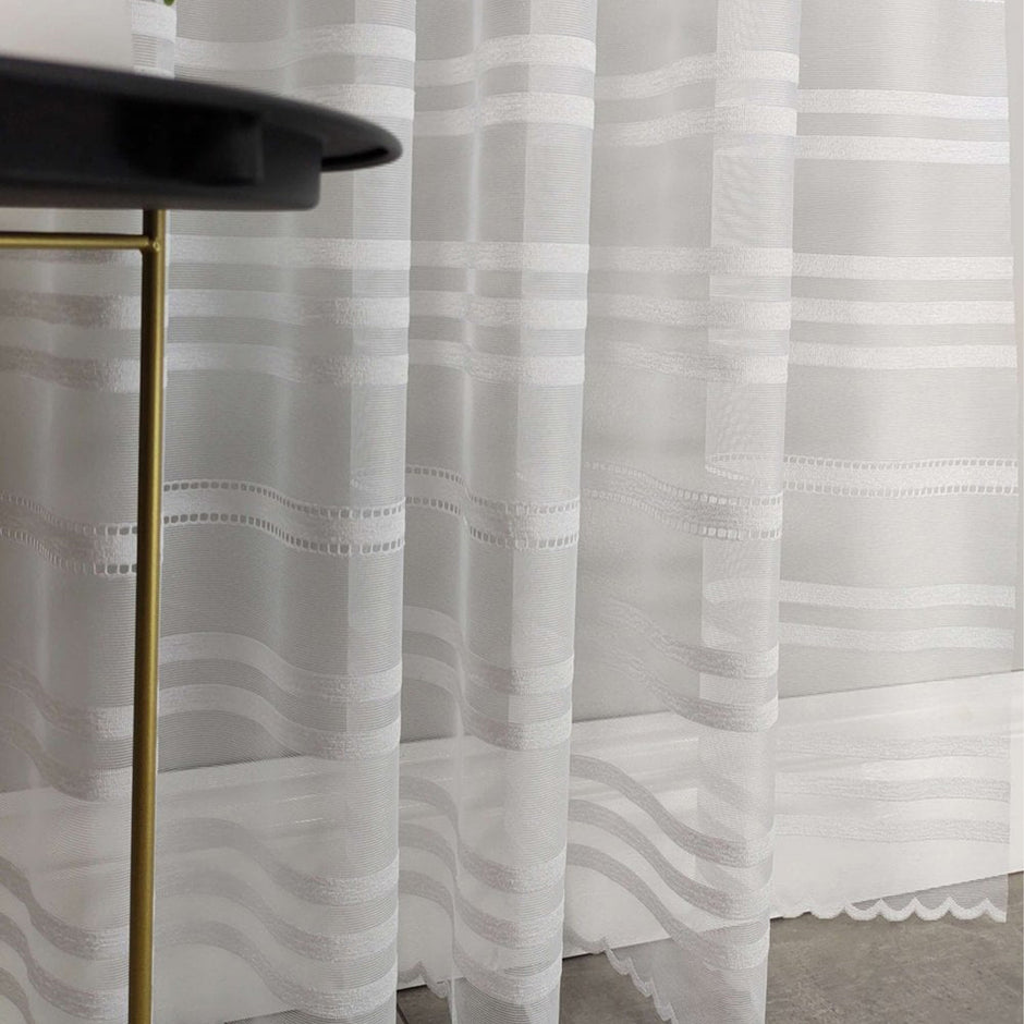 Sheer white curtain with stripe pattern in front of a black table with gold legs.