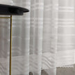 Sheer white curtain with stripe pattern in front of a black table with gold legs.