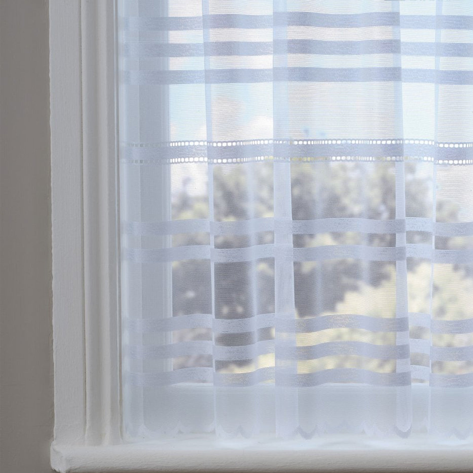 White lace curtains with horizontal sewn stripes against a window 