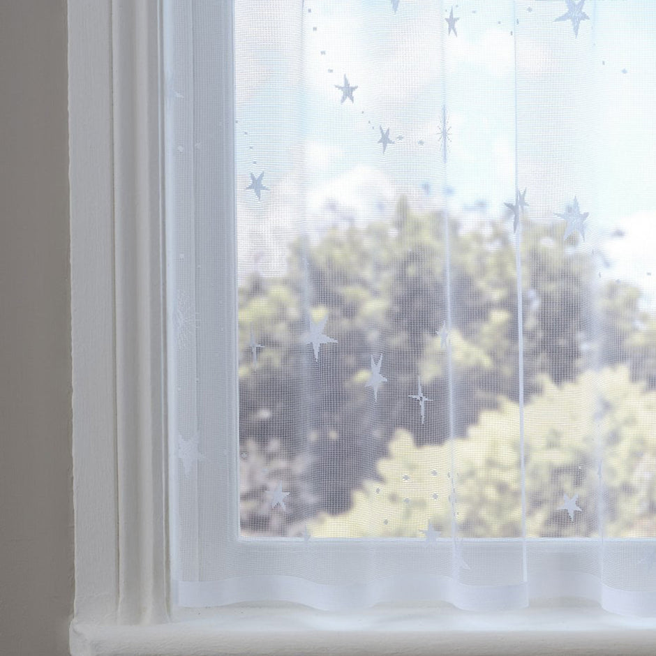 White sheer curtain with star patterns in front of a window with a view of trees.