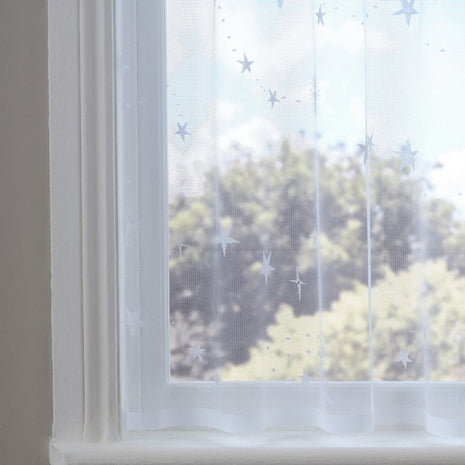 White sheer curtain with star patterns in front of a window with a view of trees.