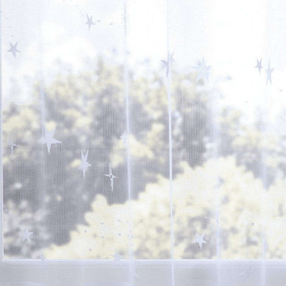 Sheer white curtain with star pattern in front of a blurred outdoor view