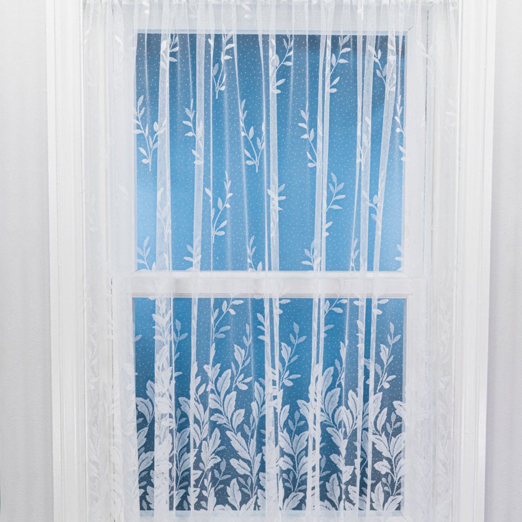 White net curtain with sewn vertical leaves against a window and blue background