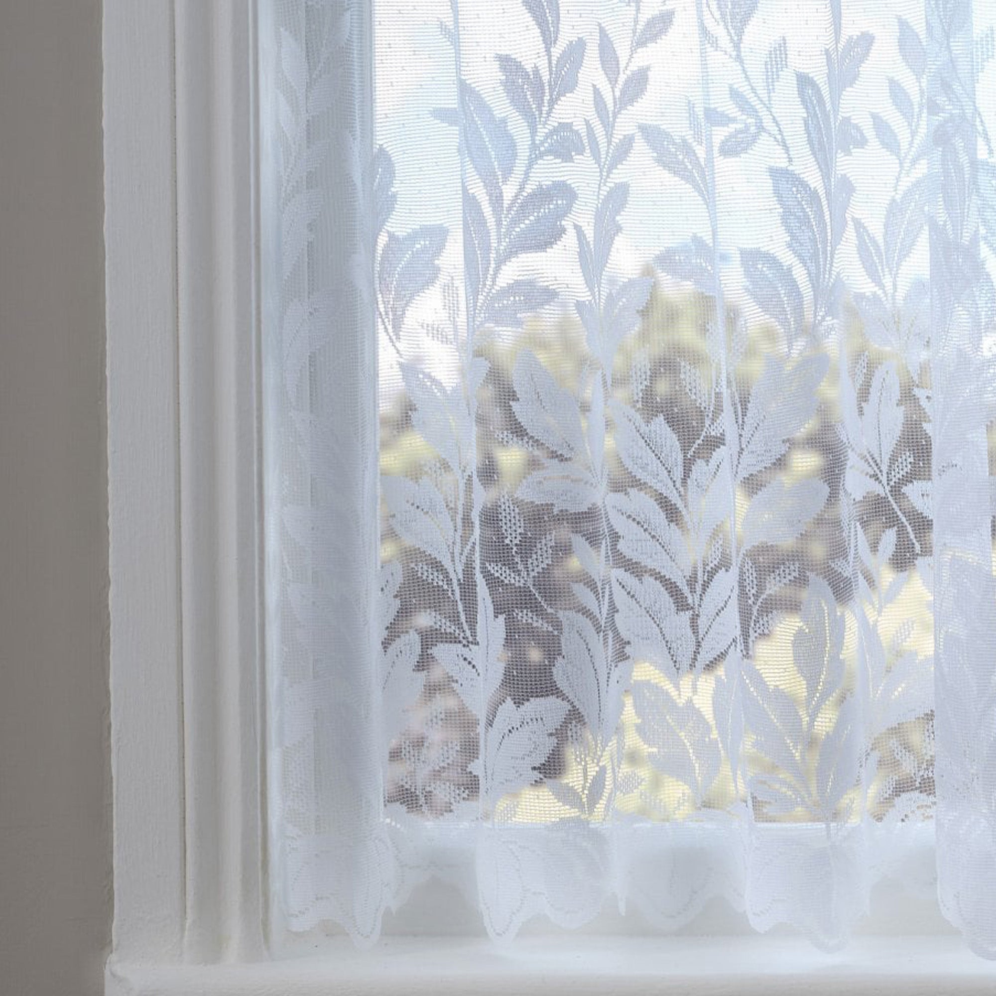 Sheer white curtain with vertical leaf pattern in front of a window