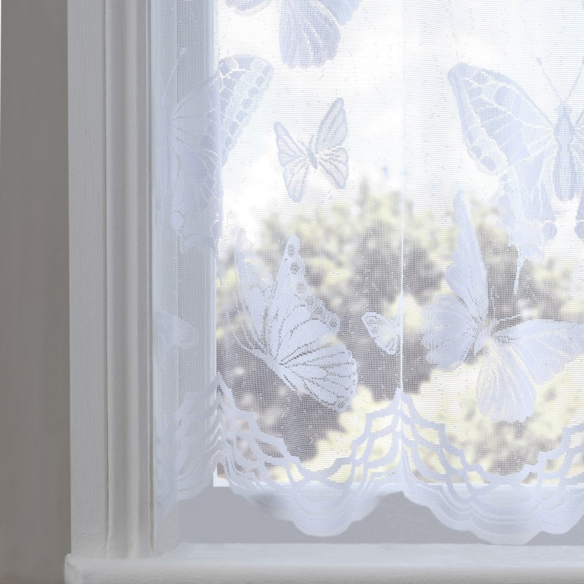 White lace curtain with butterfly patterns in front of a window