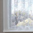 White net curtain with embroidered flowers against a window 